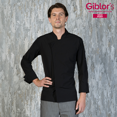 Giovane uomo con giacca da chef nera e pantaloni grigi davanti a parete testurizzata con logo Giblor's in alto a destra